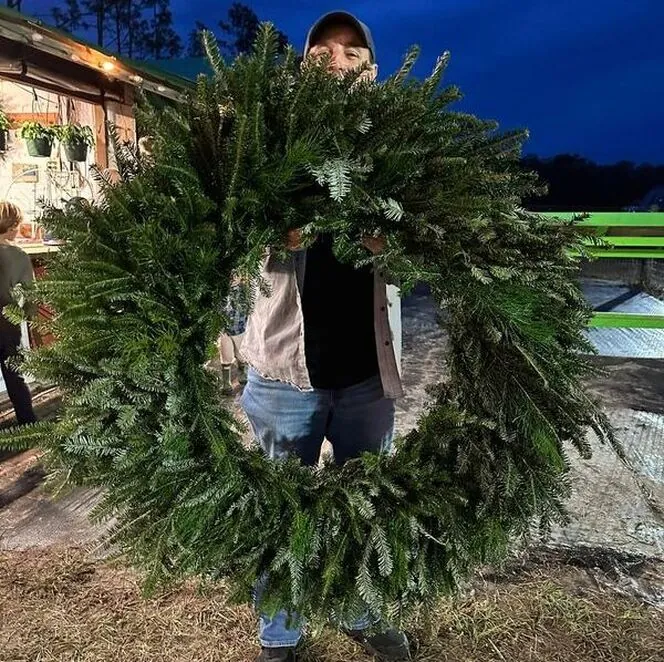 Person holding a large fresh wreath at dusk